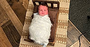 Isaiah is registered to the contest to win money with this photo: newborn, baby, swaddled, wooden_bed, pillow, rug, wood_floor, carpet, indoor, baby_wrap, portrait, infant, cute, resting, cozy, small_bed, flooring, warm, child, sleeping_area