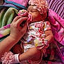 baby, newborn, sleeping, pacifier, hand, flower_headband, floral_outfit, mittens, socks, blanket, colorful, soft_texture, infant, cute, resting, toddler, person, bed, comfort, peaceful