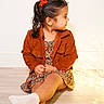 Amelia joined the competition — help win amazing prizes! child, girl, portrait, sitting, indoors, smiling, profile, hair_bow, ponytail, floral_dress, jacket, corduroy, socks, fashion, fairy_lights, wooden_floor, white_wall, studio, warm_lighting, full_body