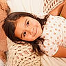 Amelia is registered to the contest to win money with this photo: child, girl, toddler, portrait, smiling, lying_down, indoors, blanket, knitted_blanket, cozy, bed, teddy_bear, brown_hair, long_hair, floral_clothing, strawberry_pattern, warm_lighting, relaxed, home, close_up