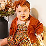 Melody is registered to the contest to win money with this photo: baby, child, infant, portrait, smiling, sitting, headband, bow, jacket, dress, floral_pattern, fairy_lights, flowers, bouquet, indoor, home, wall, floor, warm_lighting, fashion