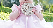Melody joined the competition — help win amazing prizes! baby, infant, child, portrait, pink_dress, headband, bow, outdoor, garden, sunlight, wooden_sign, milestone, hand, smiling, face, sitting, fashion, nature, blurred_background, photography