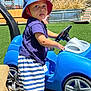 toddler, child, toy_car, blue_hat, striped_shorts, barefoot, outdoor, grass, playground, steering_wheel, sunny, summer, casual_clothing, plastic_toy, young_child, daytime, greenery, fun, curious, park