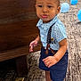 toddler, child, barefoot, blue_shirt, suspenders, navy_shorts, carpet, wooden_furniture, balloons, indoor, pout, standing, cute, expression, modern_chair, playful, person, clothing, floor, room