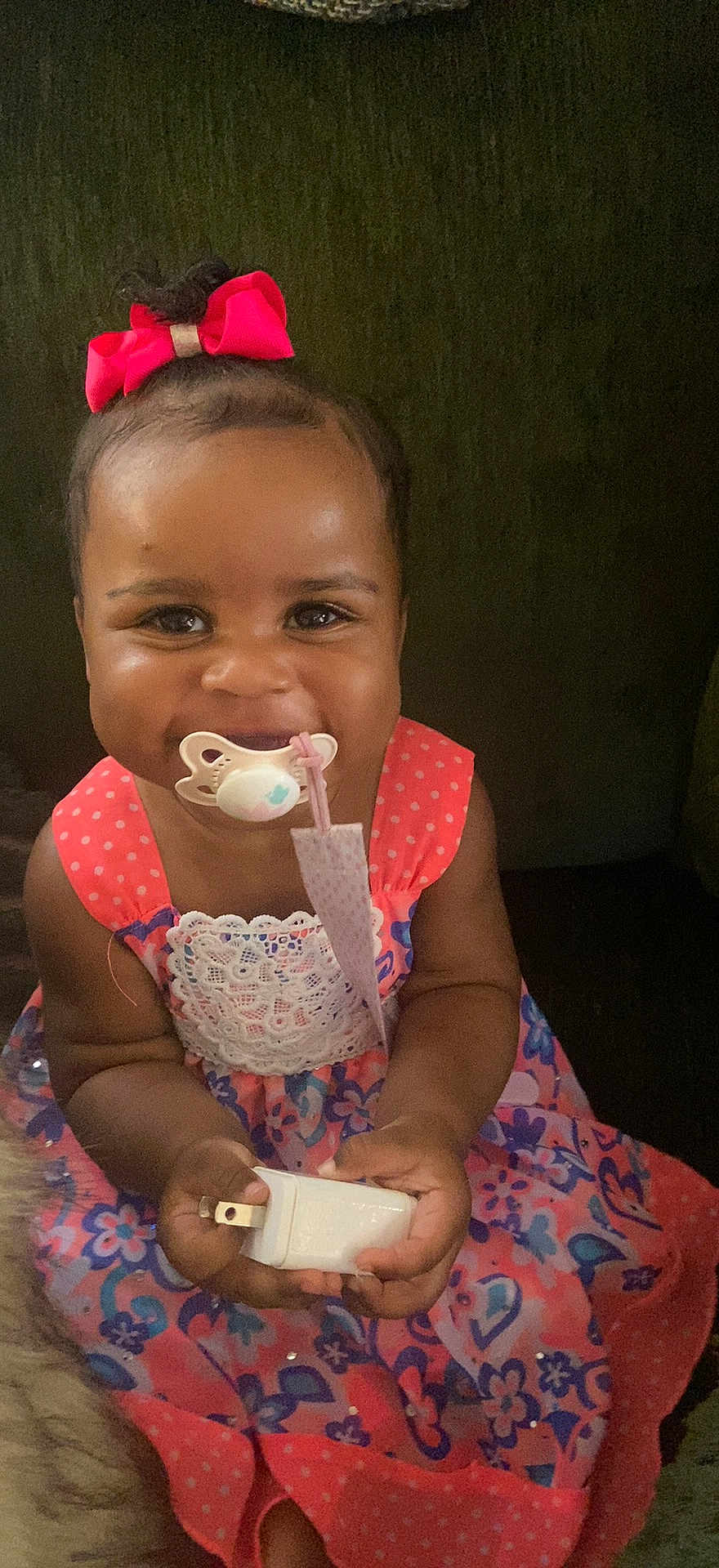 Dalaney is registered to the contest to win money with this photo: accessory, baby, child, colorful, couch, cute, dress, face, happy, holding, indoor, pacifier, person, pink_bow, plug_adapter, portrait, sitting, smile, toddler, young_child