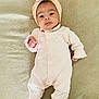 baby, infant, onesie, headband, blanket, beige, pink, lying_down, face, eyes, hand, feet, sock, portrait, indoors, cute, soft_texture, newborn, child, smile