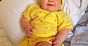 Stella is registered to the contest to win money with this photo: baby, child, yellow_clothing, headband, smile, bed, pillow, blanket, infant, cute, indoors, happy, person, portrait, sitting, soft_texture, comfortable, bright_colors, young_child, casual