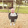 baby, swing, playground, child, grass, woodchips, trees, picnic_table, smiling, happy, outdoor, park, daylight, clothing, sock, seat, metal_chain, nature, person, fun