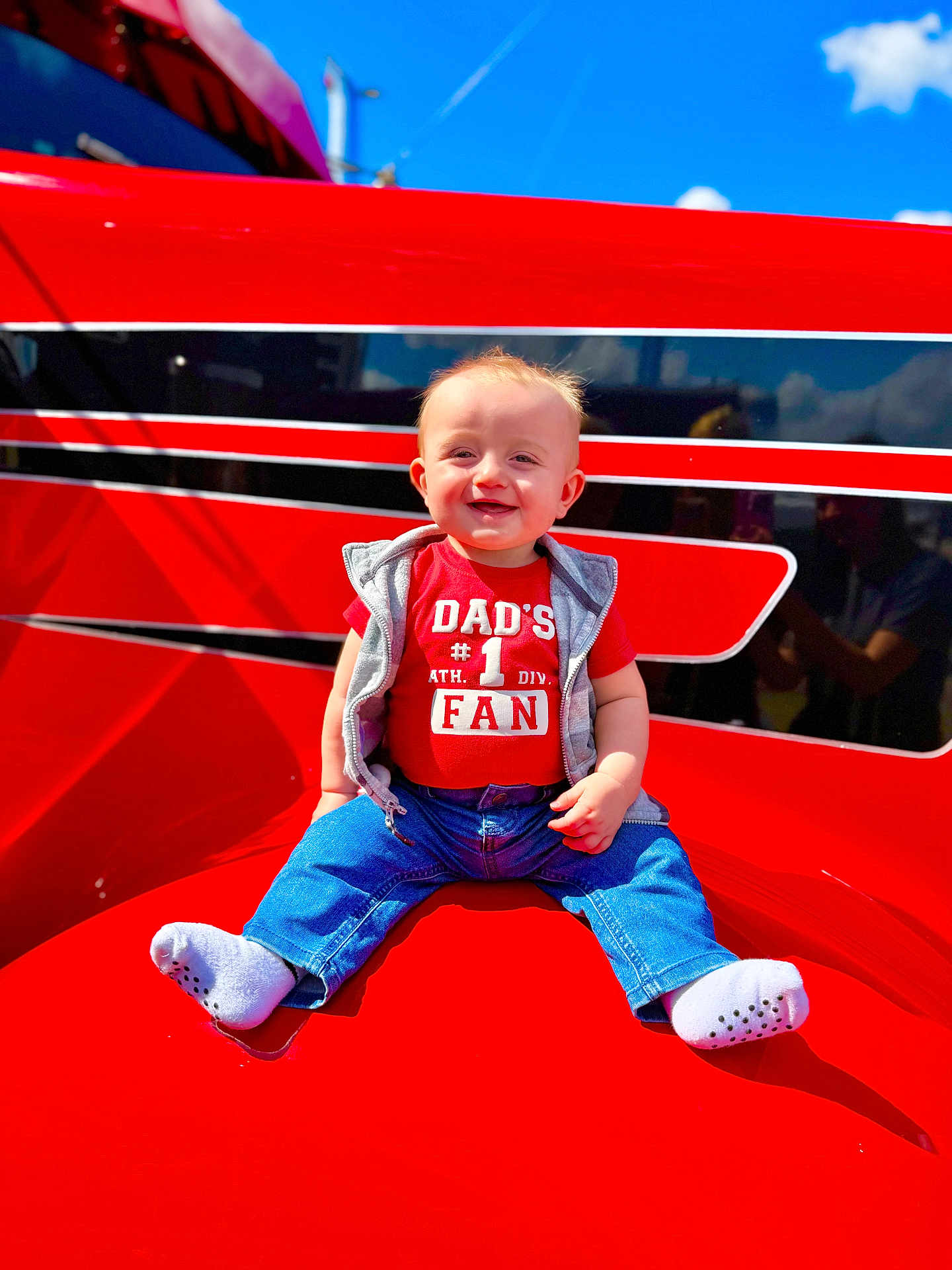 Heston joined the competition — help win amazing prizes! baby, child, red_shirt, jeans, socks, smiling, outdoor, sunny, blue_sky, clouds, red_surface, casual_clothing, happy, portrait, sitting, cute, young_child, daylight, face, person