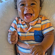 Brooks joined the competition — help win amazing prizes! baby, child, infant, smiling, laughing, curly_hair, portrait, sitting, striped_clothing, orange_clothing, blue_details, onesie, happy, joyful, indoor, cushion, seat, close_up, hands, family_photo