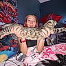 Handsome is registered to the contest to win money with this photo: woman, cat, dog, bed, blanket, spiderman, poster, bracelet, watch, phone, pillow, room, animal, pet, feline, canine, colorful, indoor, young_adult, holding