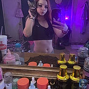 Handsome is registered to the contest to win money with this photo: woman, cat, mirror, selfie, bedroom, purple_lighting, bottle, container, dresser, clock, door, clothing, table, phone, long_hair, tabby_cat, facial_expression, indoor, reflection, casual