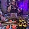woman, cat, mirror, selfie, bedroom, purple_lighting, bottle, container, dresser, clock, door, clothing, table, phone, long_hair, tabby_cat, facial_expression, indoor, reflection, casual