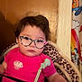 Neala is registered to the contest to win money with this photo: toddler, child, indoor, glasses, pink_shirt, cupcake_patch, leopard_print, cushion, chair, curtain, cartoon, face, person, baby, clothing, hand, hair, expression, toy, seat