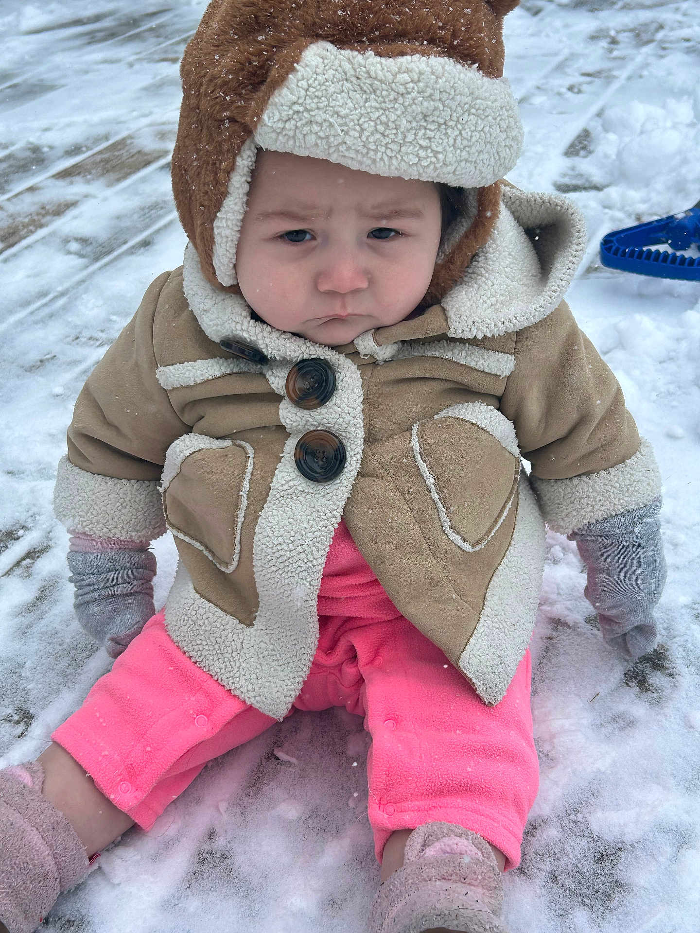 Neala is registered to the contest to win money with this photo: toddler, child, snow, winter_clothing, jacket, hood, mittens, pink_pants, boots, outdoor, cold, frown, sitting, snowy_ground, winter, cute, baby, cold_weather, fleece, expression