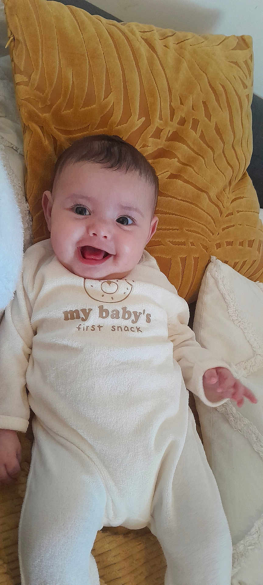 Myriam a rejoint le concours — aidez-le/la à gagner de superbes lots ! baby, smiling, onesie, pillow, yellow_pillow, white_clothing, infant, happy, couch, face, child, lying_down, indoors, cute, expression, hand, soft_texture, cozy, young_child, portrait