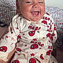 baby, blanket, child, closeup, cute, face, happy, indoor, infant, onesie, patterned_clothing, portrait, red, sitting, smiling, spiderman, superhero, tongue_out, white, young