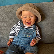 Maël Roux participe au concours pour gagner de l'argent avec cette photo : toddler, child, smiling, hat, bucket_hat, denim_overalls, striped_shirt, sitting, couch, indoor, happy, portrait, baby, face, clothing, furniture, skin, person, casual, cute