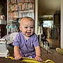 baby, child, smiling, purple_shirt, indoor, toy, furniture, shelf, blurred_background, happy, person, face, hands, playful, home, young_child, cute, infant, toddler, yellow_object