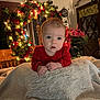 baby, infant, blanket, red_clothing, holiday_wreath, christmas_lights, indoor, decorations, plant, table, wooden_chair, face, expression, cozy, festive, home, portrait, child, cute, warm_lighting