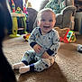 baby, smiling, pajamas, carpet, living_room, armchair, blanket, toys, dog, floor, window, natural_light, child, happy, indoor, cute, playful, pet, furniture, cozy