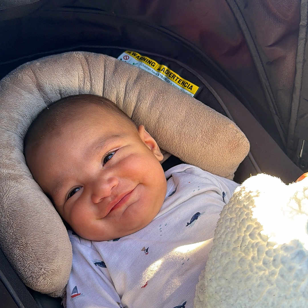 Jesús Ali is registered to the contest to win money with this photo: baby, blanket, car_seat, child, clothing, cushion, face, happy, head, indoors, infant, person, portrait, seat, sitting, smile, soft_texture, toddler, warm, young