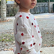 Saona participe au concours pour gagner de l'argent avec cette photo : child, toddler, outdoor, tree, fence, apple_pattern, white_clothing, long_sleeve, pants, curly_hair, standing, side_profile, expression, nature, ground, concrete, leaves, daylight, casual, portrait