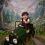 baby, child, toy_car, vintage_clothing, cap, smiling, indoor, portrait, green, grass, trees, flowers, scenic_background, pathway, playful, happy, retro, classic, footwear_bare, studio_photo