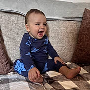 Oakley is registered to the contest to win money with this photo: toddler, child, smiling, laughing, blue_clothing, stars_pattern, sitting, couch, blanket, pillows, indoors, happy, baby, foot, hand, face, cozy, home, portrait, casual