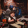 toddler, child, smile, hat, vest, wrench, tires, tools, can, toy_car, garage, brick_wall, workshop, vintage, retro, clothing, floor, sitting, happy, portrait