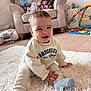 baby, child, sitting, smiling, indoor, rug, cozy, sweatshirt, sock, toy, plush, furniture, carpet, living_room, cute, young_child, happy, face, person, home
