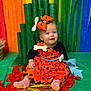 baby, child, costume, orange_dress, bow, bone_accessory, pink_socks, smiling, sitting, colorful_background, rainbow, decorations, festival, celebration, happy, portrait, indoors, cute, playful, festive