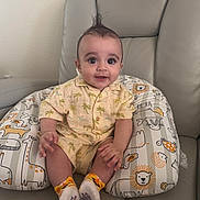 Dylan is registered to the contest to win money with this photo: baby, child, infant, smiling, sitting, pillow, animal_print, leather_chair, yellow_outfit, short_sleeves, socks, cute_hair, indoors, happy, portrait, young_child, palm_tree_pattern, hand, skin, furniture