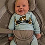 Tommy is registered to the contest to win money with this photo: baby, smiling, infant, blue_clothing, moschino, teddy_bear, baby_seat, straps, happy, cute, child, indoor, face, head, person, seat, comfort, relaxed, small_hands, footwear