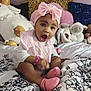 Beyon is registered to the contest to win money with this photo: baby, child, pink_bow, socks, bedspread, stuffed_animals, plush_toys, indoor, happy, cute, smiling, portrait, headwear, pink, white_clothing, bedroom, decor, toy, sitting, young_child