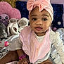 baby, child, pink_bow, headband, bib, bracelet, plush_toys, bed, blanket, pillow, stuffed_animal, indoor, cute, smile, sitting, person, clothing, infant, toy, portrait