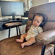 Eliana joined the competition — help win amazing prizes! baby, headphones, chair, computer_monitor, keyboard, desk, water_dispenser, onesie, home_office, infant, footwearless, couch, indoor, technology, furniture, window, curtains, relaxed, person, expression