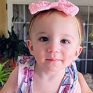 Gianna is registered to the contest to win money with this photo: baby, child, portrait, close_up, face, headband, pink_bow, butterfly_pattern, dress, sleeveless, sitting, looking_at_camera, wide_eyes, neutral_expression, indoor, home, plant, glass_door, natural_light, photography