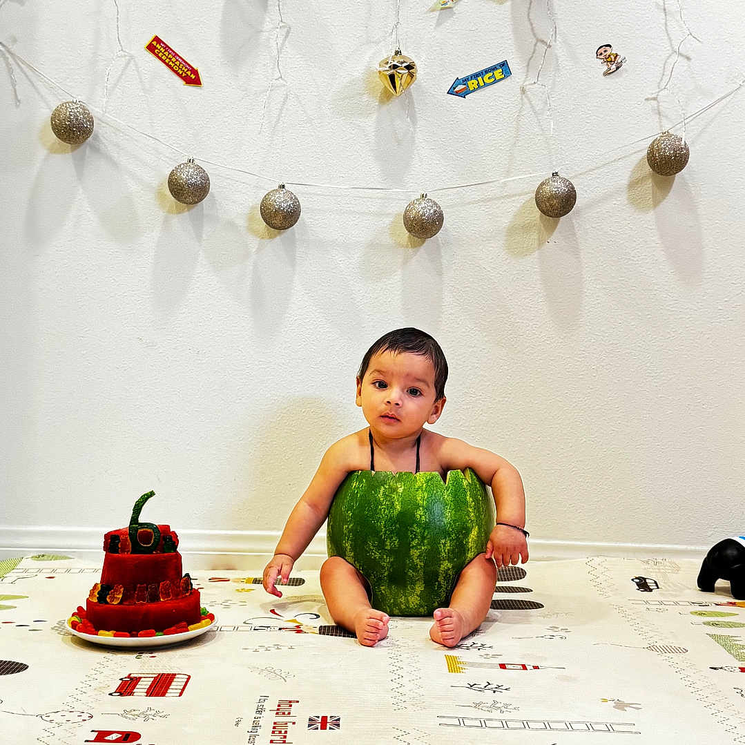 Aadvik joined the competition — help win amazing prizes! birthday, cake, celebration, child, colorful, cute, decorations, festive, floor_mat, food, fruit, indoor, ornaments, party, sitting, string_lights, toddler, wall, watermelon, young_child