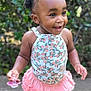 toddler, child, girl, smiling, standing, outdoor, hair_clips, pacifier, concrete, floral_top, pink_skirt, sparkly_shoes, happy, cute, person, young_child, nature, greenery, sunlight, playful
