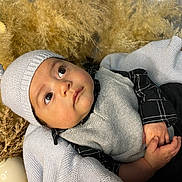 Kamillo joined the competition — help win amazing prizes! baby, child, knit_hat, sweater_vest, black_shirt, blanket, dried_plants, vase, portrait, indoors, curious, hands, face, eyes, soft_texture, cozy, warm_colors, infant, headwear, candid