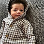 baby, infant, hooded_jacket, plaid, checkered, buttoned_clothing, lying_down, curly_hair, smile, face, hand, blanket, texture, cozy, cute, child, portrait, indoors, warm_clothing, young_child