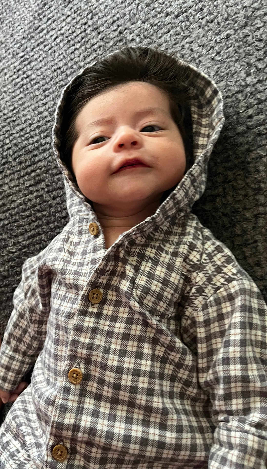 Kamillo is registered to the contest to win money with this photo: apparel, baby, buttons, child, cozy, cute, fabric, face, hair, hooded_clothing, indoors, infant, lying_down, pattern, plaid, portrait, smile, textured_surface, warm, young_child