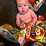 baby, child, toy, toys, mickey_mouse, plush_toy, box, packaging, couch, indoor, person, cute, chubby, infant, colorful, sitting, holding, expression, red_toy, playful