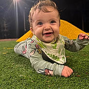 Abigail joined the competition — help win amazing prizes! baby, child, grass, night, streetlight, playground, yellow_structure, smiling, happy, clothing, bib, face, person, outdoor, cute, infant, lying_down, green, nature, eyes