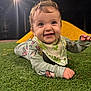 baby, child, grass, night, streetlight, playground, yellow_structure, smiling, happy, clothing, bib, face, person, outdoor, cute, infant, lying_down, green, nature, eyes