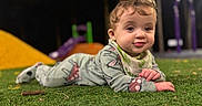 Abigail is registered to the contest to win money with this photo: baby, bib, blurred_background, child, clothing, colorful, curious, cute, expression, face, grass, infant, lying_down, night, outdoor, play, playground, soft_lighting, toy, young_child