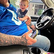 Rickey joined the competition — help win amazing prizes! baby, child, infant, smiling, happy, portrait, father, parent, family, car, truck, vehicle, steering_wheel, driver, interior, outdoor, daylight, tattoo, sports_jersey, road_trip