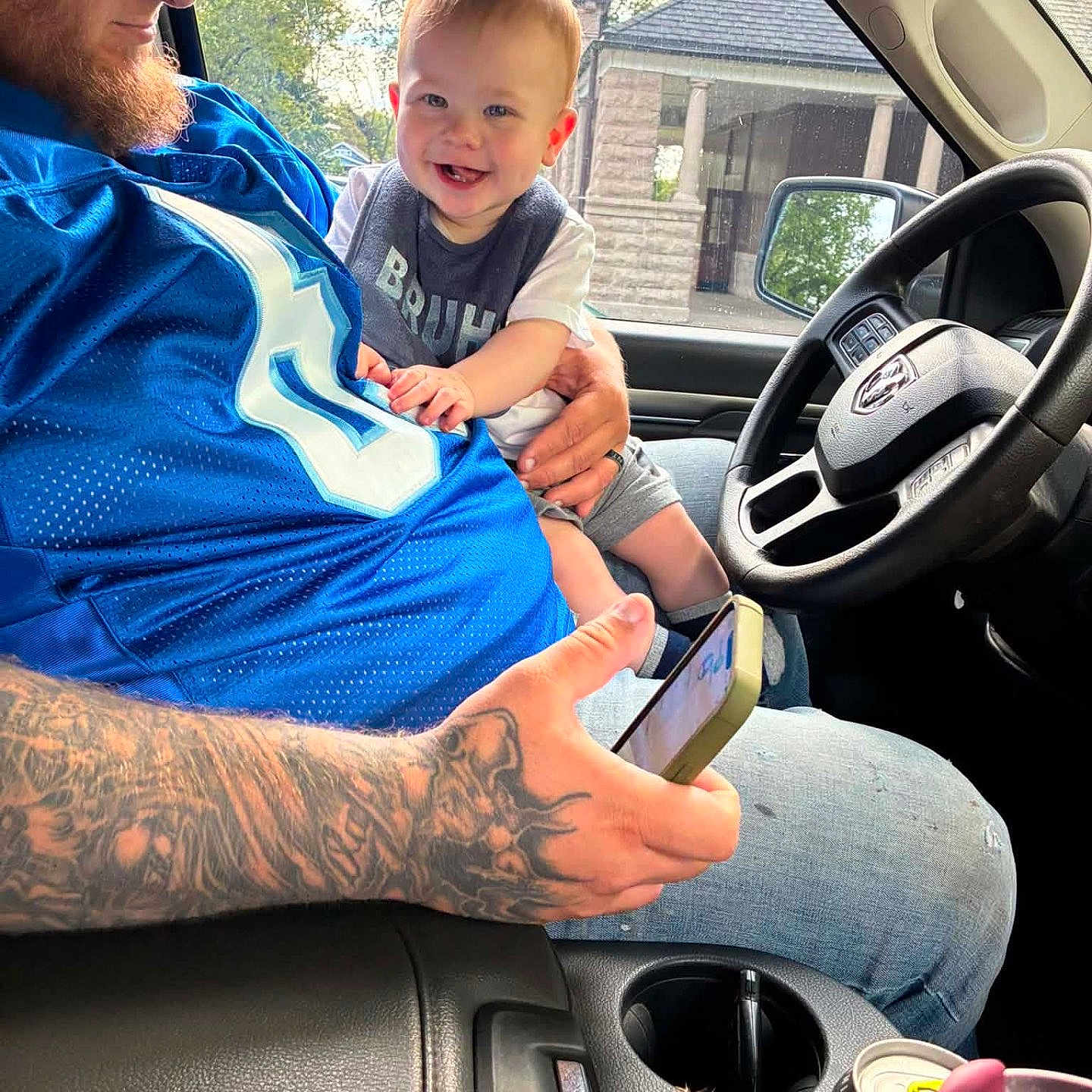 Rickey joined the competition — help win amazing prizes! baby, child, infant, smiling, happy, portrait, father, parent, family, car, truck, vehicle, steering_wheel, driver, interior, outdoor, daylight, tattoo, sports_jersey, road_trip