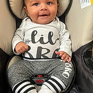 Malakai is registered to the contest to win money with this photo: baby, smiling, infant, car_seat, clothing, white_shirt, gray_pants, socks, baby_boy, happy, cute, child, face, portrait, seated, indoor, baby_fashion, baby_accessory, car_safety, closeup